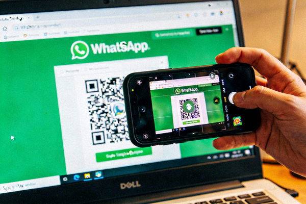 用户手持智能手机，使用摄像头扫描电脑屏幕上显示的WhatsApp网页版二维码